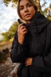 Manteau à capuche imperméable noir porté par une femme, vue rapprochée, capuche relevée, main au col