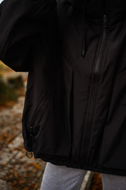 Manteau à capuche imperméable noir porté par une femme, vue rapprochée, dos du manteau, fermeture