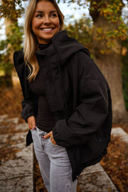 Manteau à capuche imperméable noir porté par une femme, vue de trois-quarts, capuche, sourire