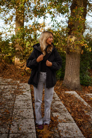 Manteau à capuche imperméable noir porté par une femme, vue de face, allée pavée, jean gris