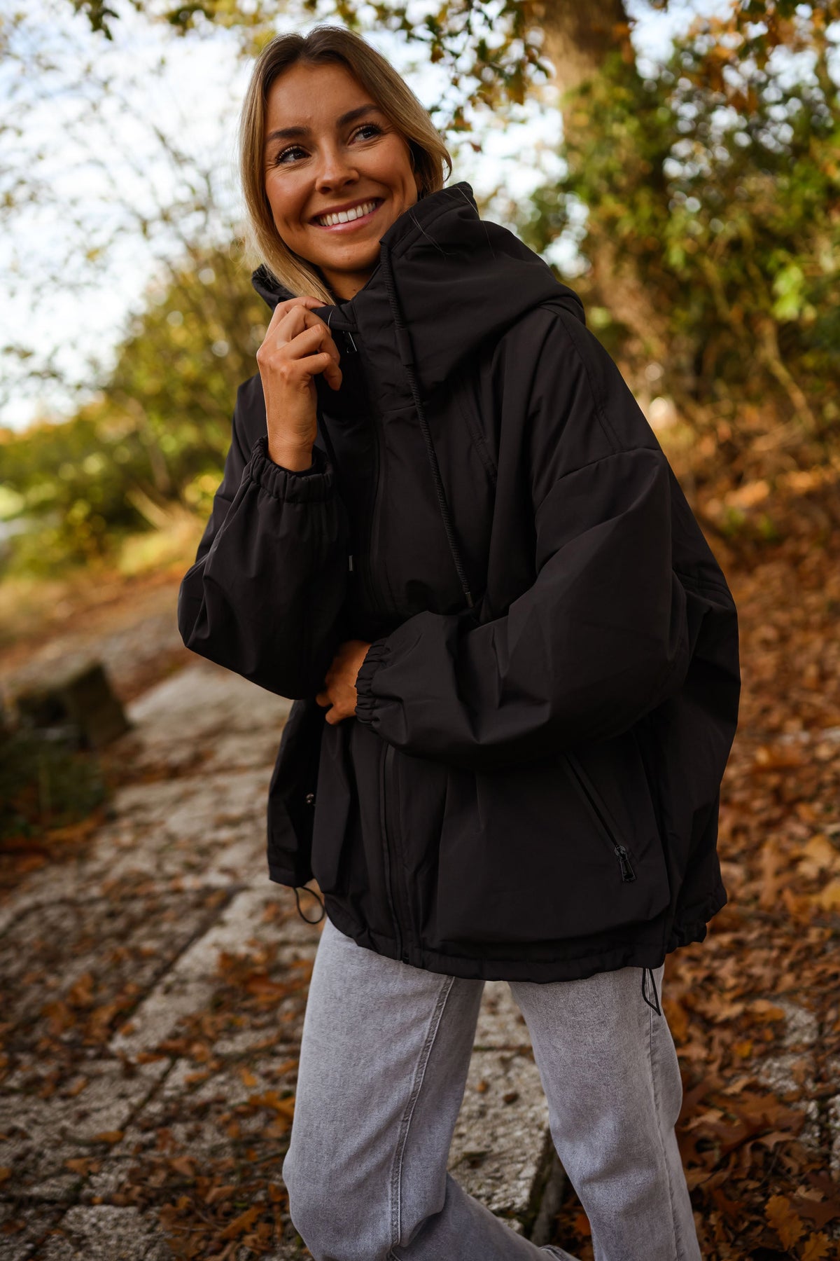 Manteau à capuche imperméable noir porté par une femme, vue rapprochée, capuche noire, main sur la capuche