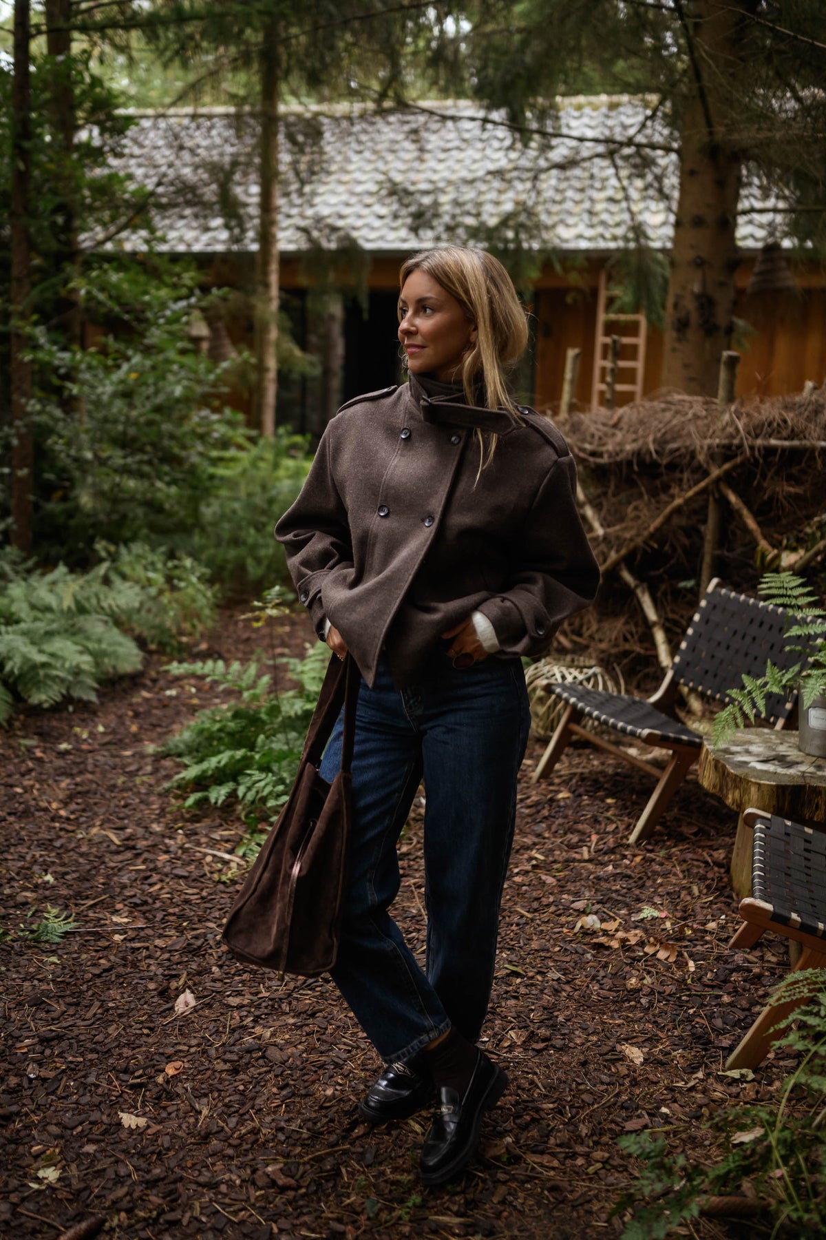 Manteau doublé à revers montant marron porté par une femme, vue de trois-quarts, sous-bois, jean bleu