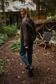 Manteau doublé à revers montant marron porté par une femme, vue de dos, sous-bois, jean bleu