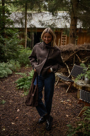 Manteau doublé à revers montant marron porté par une femme, vue de face, chaises de jardin, jean foncé