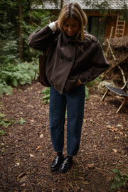 Manteau doublé à revers montant marron porté par une femme, vue de face, sous-bois, bottines noires