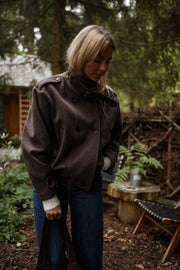 Manteau doublé à revers montant marron porté par une femme, vue de trois-quarts, chaises de jardin, cheveux blonds