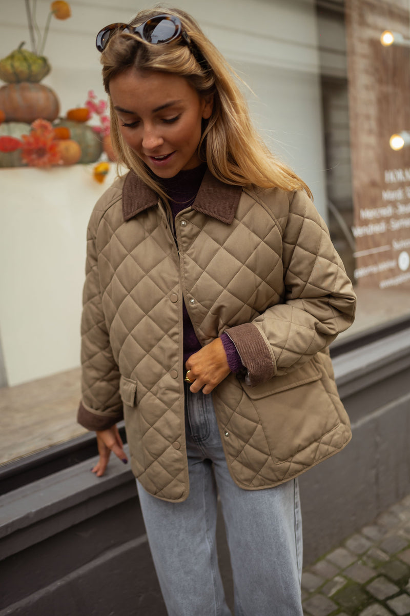 Manteau doublé à revers velours kaki porté par une femme, vue de face, lunettes de soleil sur la tête, vitrine
