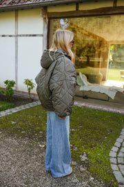 Manteau imperméable matelassé kaki porté par une femme, vue de dos, pelouse, jean bleu