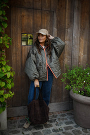 Manteau imperméable matelassé kaki porté par une femme, vue de face, porte en bois, casquette beige