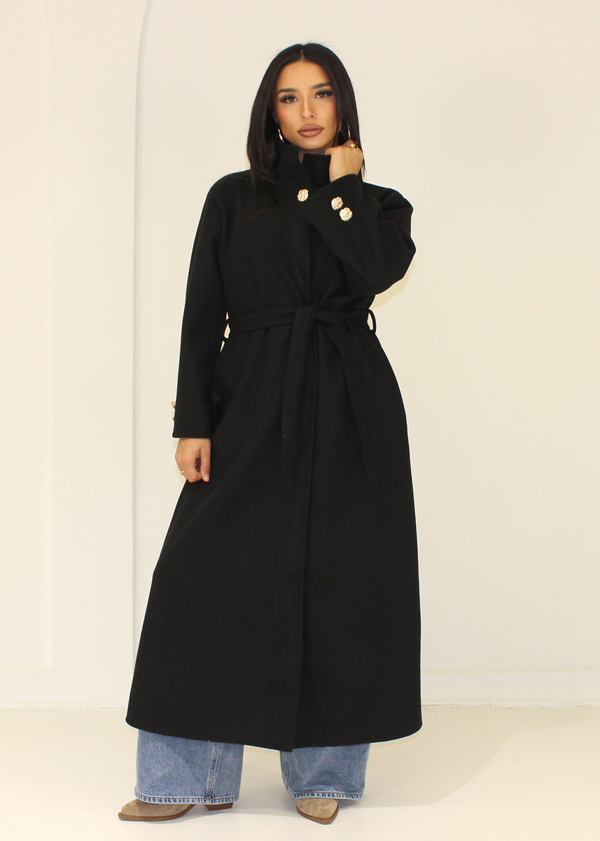 Manteau long noir à col montant — vue portée avec col relevé.