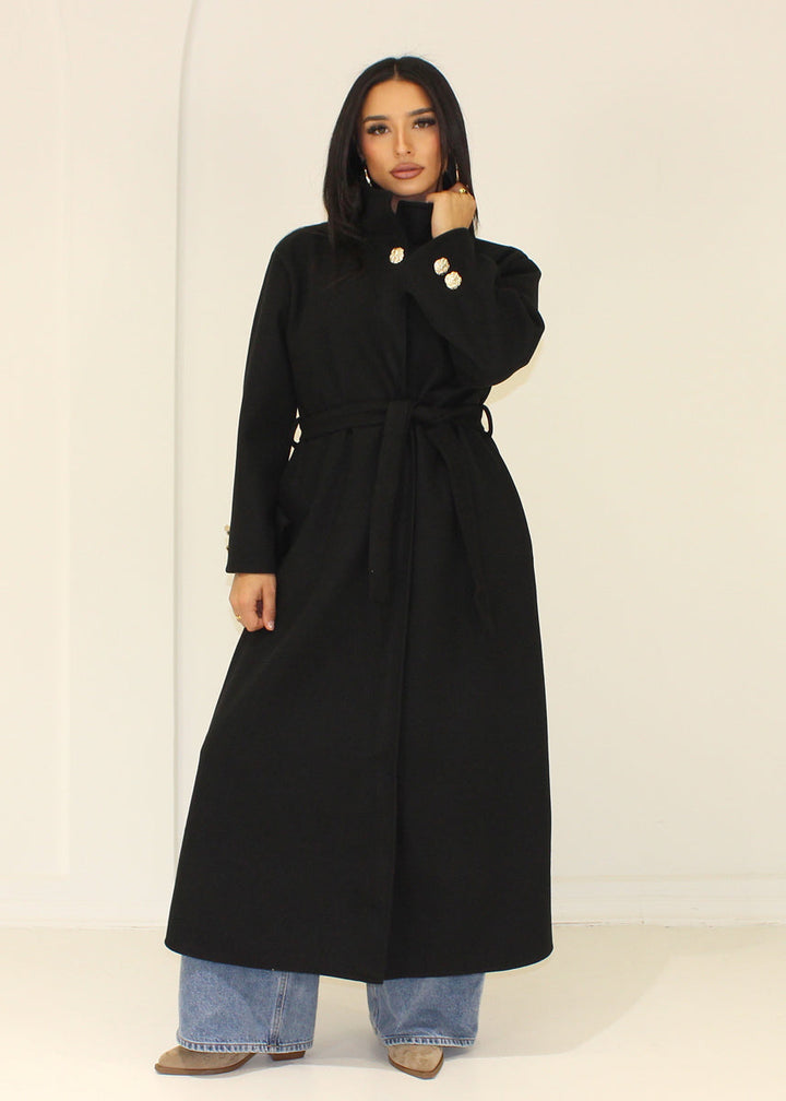 Manteau long noir à col montant — vue portée avec col relevé.