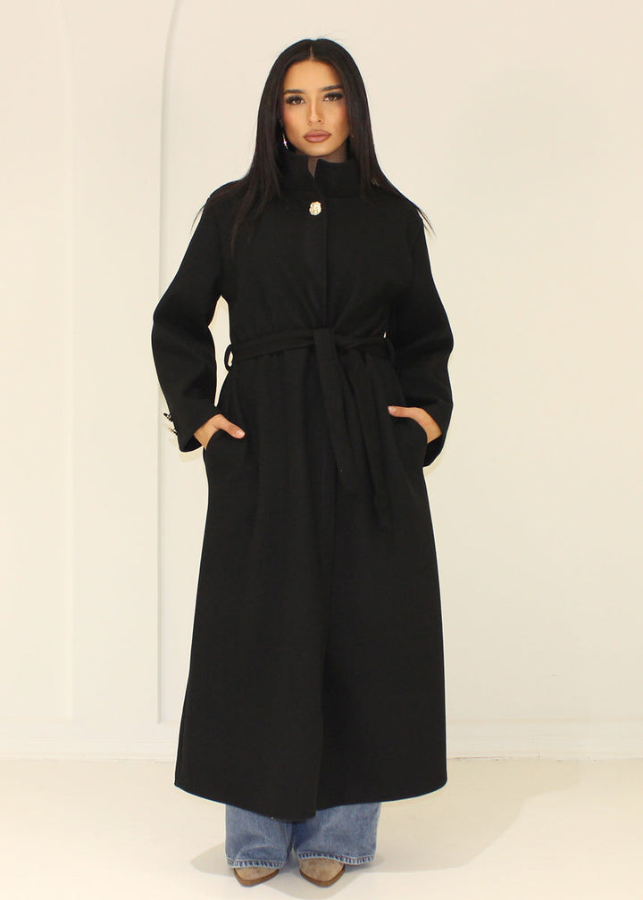 Manteau long noir à col montant — vue portée de face.