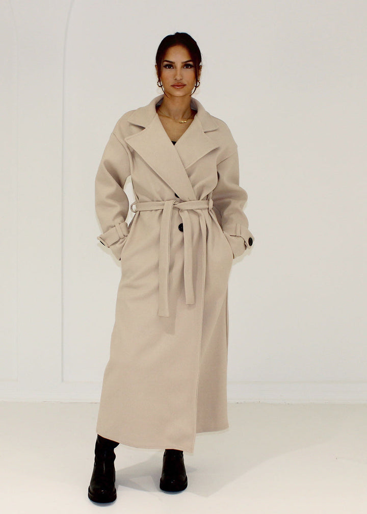 Manteau beige à double boutonnage — vue de face, ceinture nouée.