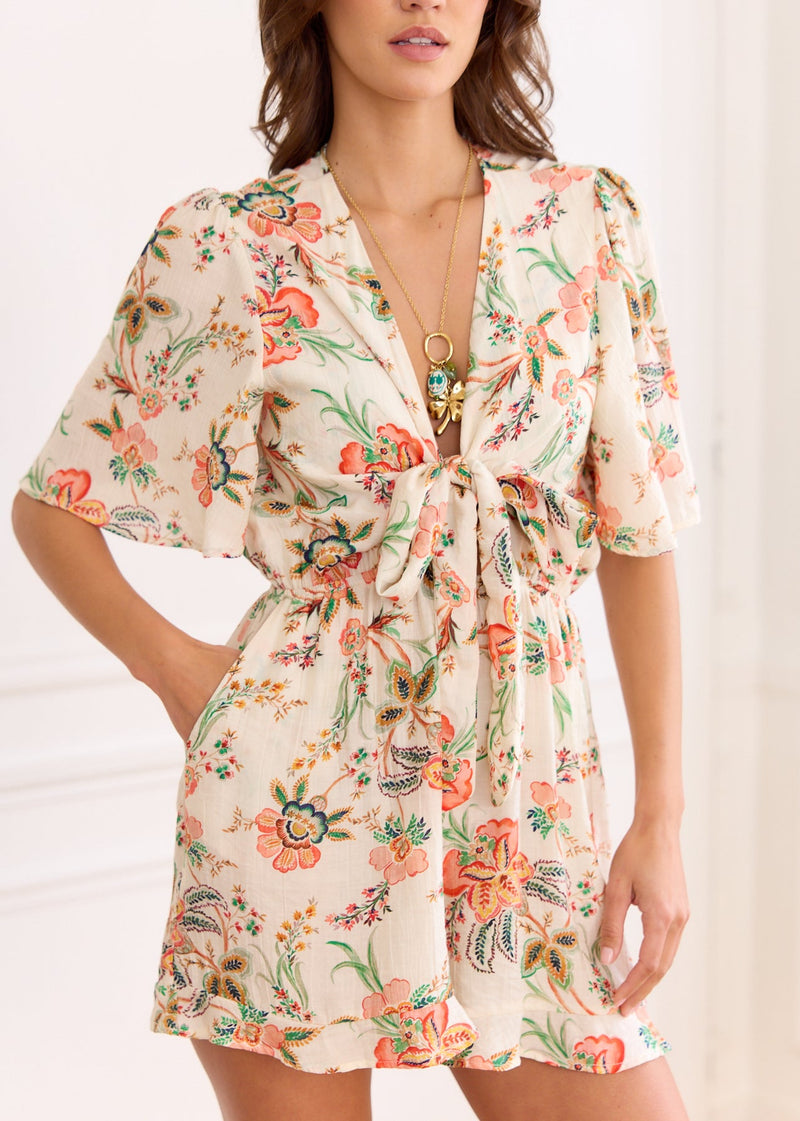 Combishort fleuri orange vert — plan mi-corps de face, nœud au col et main en poche