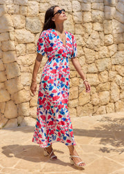 Robe longue fleurie rose et bleue, portée de trois quarts avec un décolleté en V.