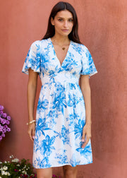 Robe courte blanche à fleurs bleues, portée de face, bras le long du corps.