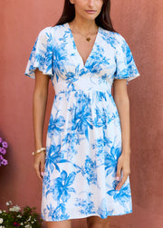 Robe blanche à fleurs bleues, décolleté en V et manches courtes évasées, portée de face.