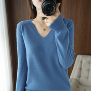 Pull col V Oriane bleu — vue portée de face, plan taille, fauteuil capitonné en fond