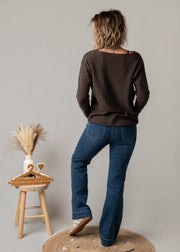 Pull col V texturé porté par une femme, vue de dos, jean flare, tabouret