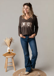 Pull col V texturé porté par une femme, silhouette entière, jean flare, tabouret
