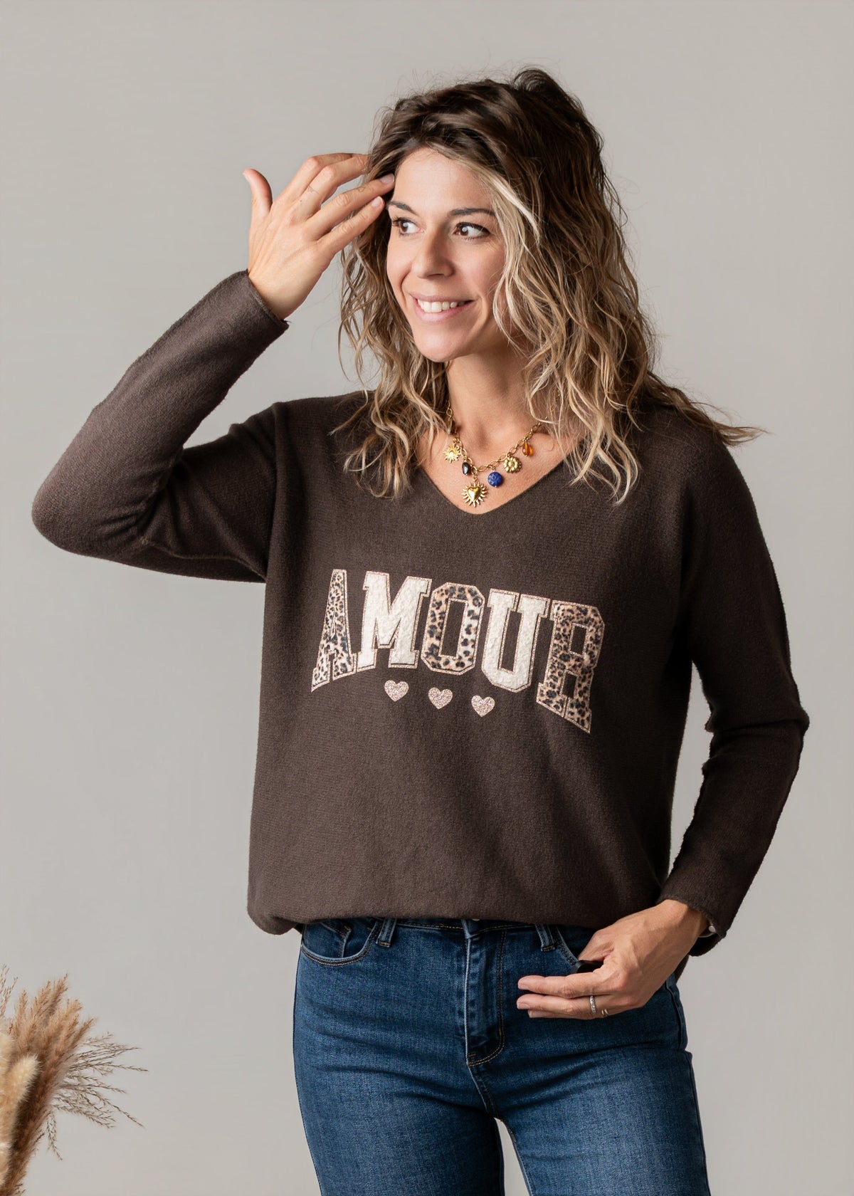 Pull col V texturé porté par une femme, vue de trois-quarts, main sur la tête, jean
