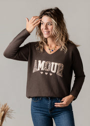 Pull col V texturé porté par une femme, vue de trois-quarts, main sur la tête, jean