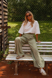 Pantalon fluide à pois porté par une femme, assise, banc blanc, plan large