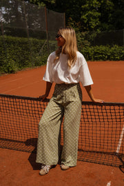 Pantalon fluide à pois porté par une femme, silhouette entière, filet de tennis, t-shirt blanc