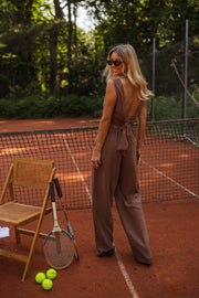 Pantalon fluide en lin chocolat porté par une femme, vue de dos, chaise, sac