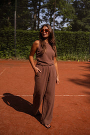 Pantalon fluide en lin chocolat porté par une femme, silhouette entière, court de tennis
