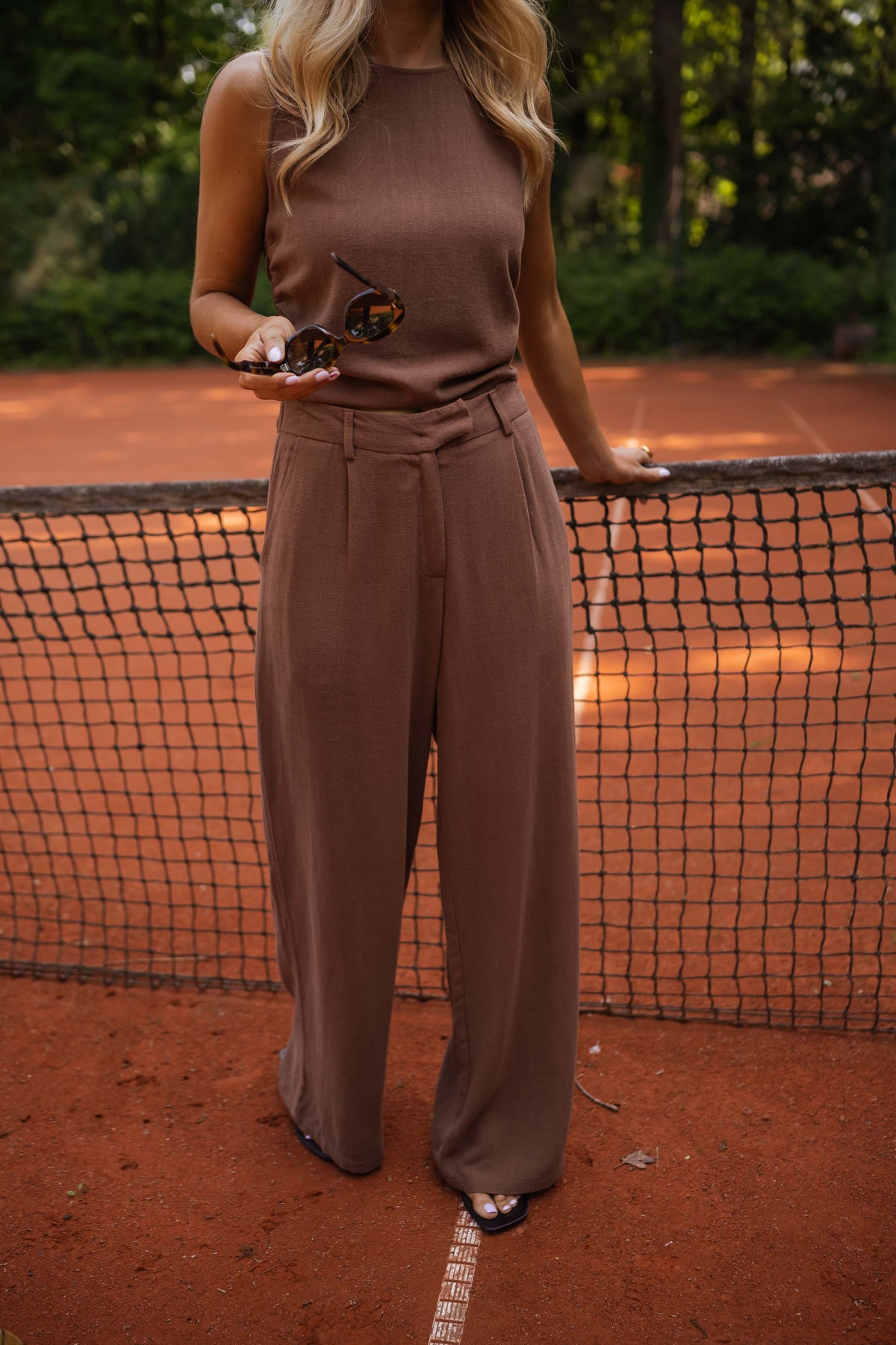 Pantalon fluide en lin chocolat porté par une femme, vue rapprochée, ensemble marron, filet de tennis