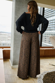 Pantalon fluide léopard porté par une femme, vue de dos, mains sur les hanches, haut noir