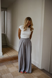 Pantalon à pinces rayé loose porté par une femme, vue de trois-quarts, haut blanc, mur