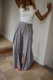 Pantalon à pinces rayé loose porté par une femme, silhouette entière, haut blanc, mur