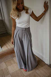 Pantalon à pinces rayé loose porté par une femme, vue de trois-quarts, main sur le mur