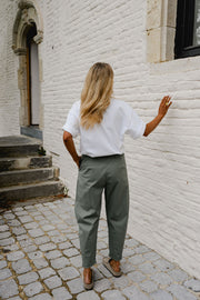 Pantalon barrel légèrement court porté par une femme, silhouette entière, t-shirt blanc, mur