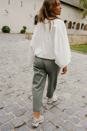 Pantalon barrel légèrement court porté par une femme, vue de dos, blouse blanche, pavés