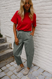 Pantalon barrel légèrement court porté par une femme, silhouette entière, haut rouge, mur blanc