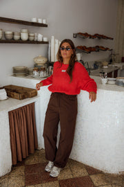 Pantalon cargo à poches latérales porté par une femme, silhouette entière, pull rouge, comptoir, de face