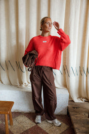 Pantalon cargo à poches latérales porté par une femme, silhouette entière, pull rouge, banc