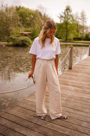 Pantalon fluide en lin beige porté par une femme, silhouette entière, étang, ponton