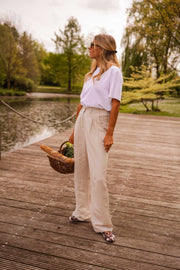 Pantalon fluide en lin beige porté par une femme, silhouette entière, étang, panier