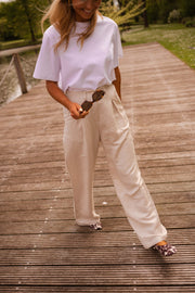 Pantalon fluide en lin beige porté par une femme, vue de trois-quarts, ponton, main à la ceinture