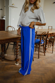Pantalon à bandes et cordon porté par une femme, silhouette entière, table en bois, parquet