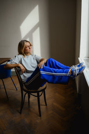 Pantalon à bandes et cordon porté par une femme, assise sur une chaise, jambes étendues