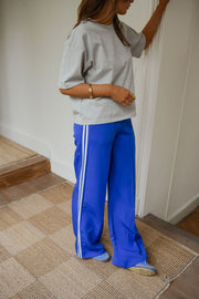 Pantalon à bandes et cordon porté par une femme, vue de trois-quarts, mur blanc, bras levé