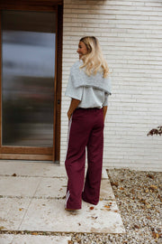 Pantalon à bandes latérales porté par une femme, vue de dos, mur blanc, de loin