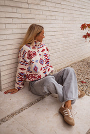 Polaire zippée à motifs écrue portée par une femme, assise, mur blanc, baskets