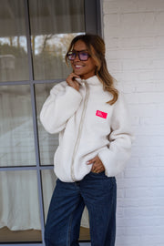 Polaire doublée à col montant portée par une femme, vue de face, porte vitrée, lunettes de soleil