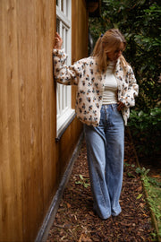 Veste polaire fleurie zippée écru portée par une femme, vue de trois-quarts, mur en bois, fenêtre blanche